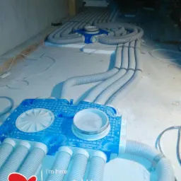 Rozdzielacz rekuperacji z podłączonymi przewodami wentylacyjnymi, widoczne elementy systemu rozprowadzone na podłodze w trakcie montażu.