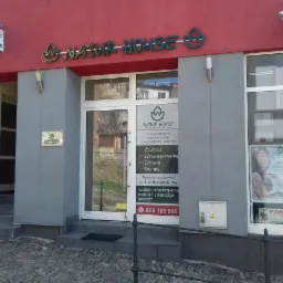 Fasada budynku Natur House z szyldem i plakatem reklamowym, oferującego konsultacje dietetyczne i poprawę sylwetki, widoczny numer telefonu.