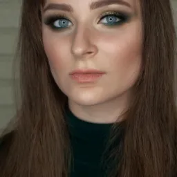 Portret kobiety z zielono-złotym makijażem oczu i długimi, prostymi, brązowymi włosami w ciemnozielonym golfie.