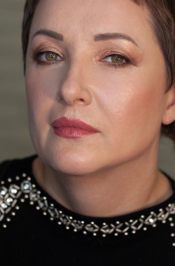 Portret kobiety z delikatnym, profesjonalnym makijażem: złote cienie do powiek i różowe usta, z uwzględnieniem cery dojrzałej.