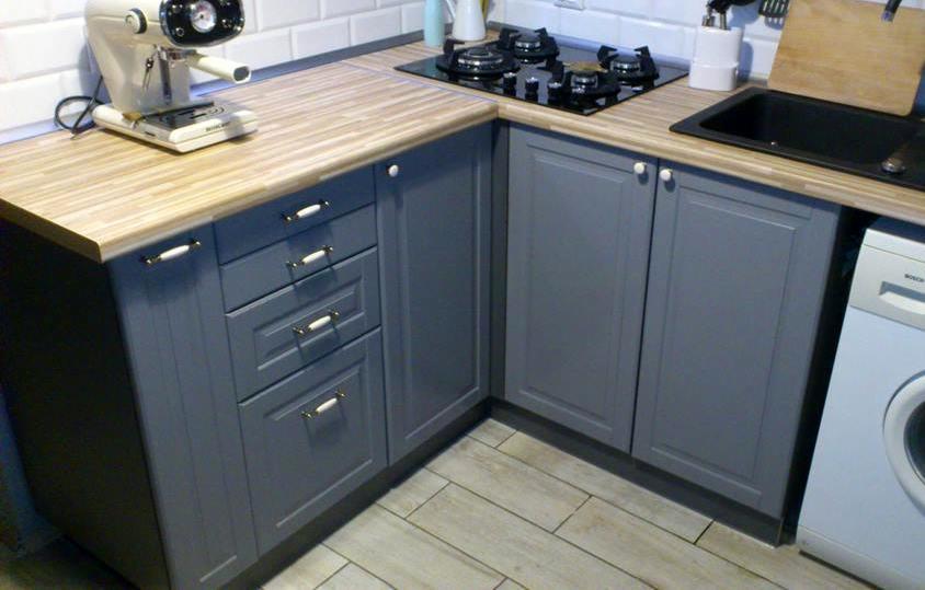 Szare szafki kuchenne z drewnianym blatem, widoczna płyta gazowa, zlew i ekspres do kawy.