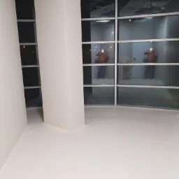 Jasna, pusta przestrzeń biurowa z nową podłogą o drobnej fakturze; widoczne okna z odbiciem osoby robiącej zdjęcie.