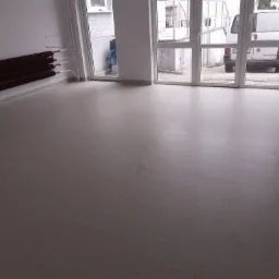 Jasnoszara, świeżo położona wykładzina w pustym pomieszczeniu z grzejnikiem na ścianie i widokiem na samochód dostawczy za oknem.