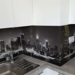 Szklany panel kuchenny z czarno-białym motywem panoramy Nowego Jorku, zamontowany między blatem a szafkami, widoczny zlew ze stali nierdzewnej.