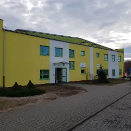 Dwukondygnacyjny budynek z żółto-białą elewacją i zielonymi ramami okiennymi, widoczny z zewnątrz, z pracującym na podnośniku hydraulicznym pracownikiem w pomarańczowym kombinezonie, prawdopodobnie...