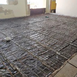 Zbrojenie pod wylewkę na folii, widoczne betonowe dystanse, częściowo wykończone pomieszczenie w tle.