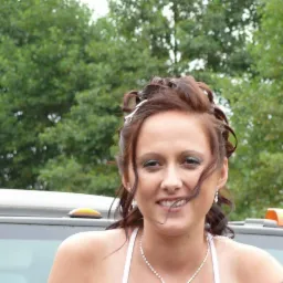 Portret uśmiechniętej kobiety z upiętymi włosami, delikatnym makijażem i biżuterią na tle zieleni.