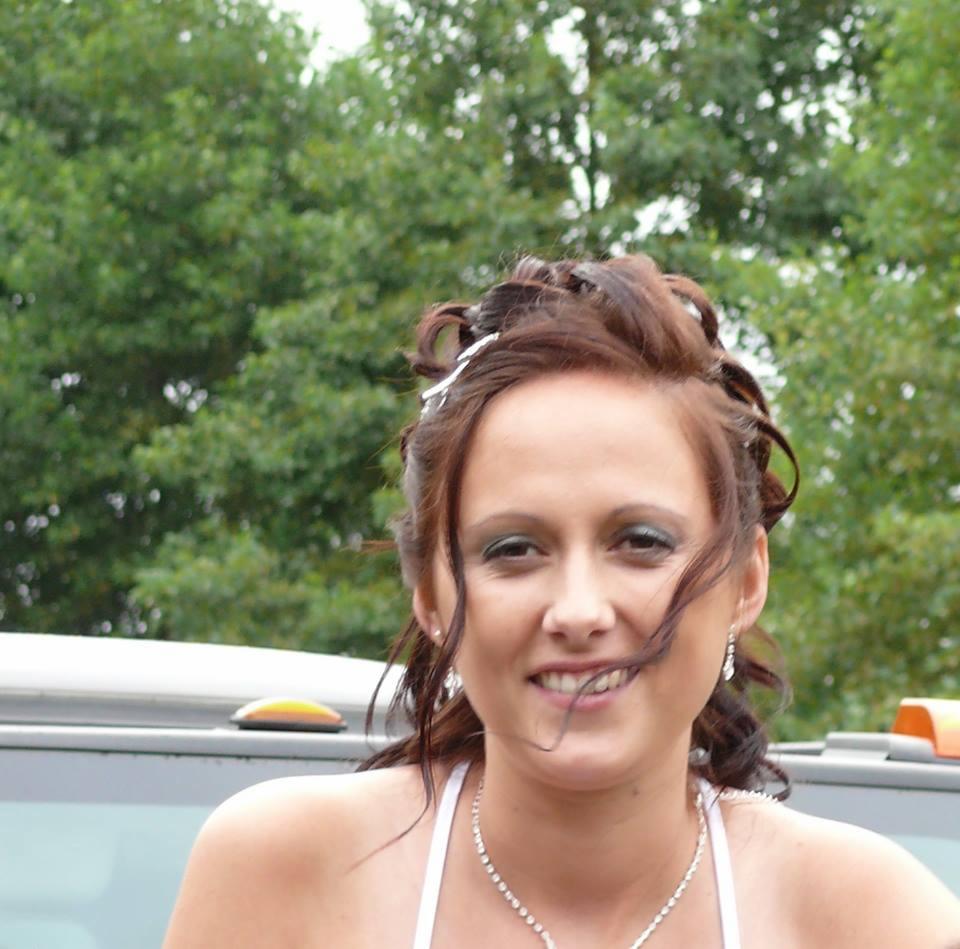 Portret uśmiechniętej kobiety z upiętymi włosami, delikatnym makijażem i biżuterią na tle zieleni.