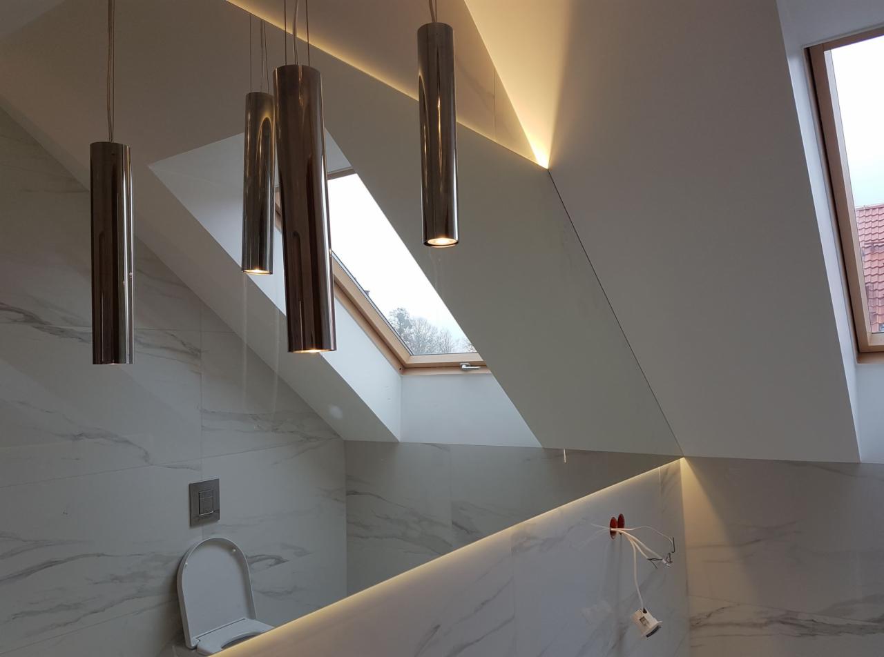 Nowoczesna łazienka na poddaszu z marmurowymi płytkami, oświetleniem LED i cylindrycznymi lampami wiszącymi, widok na okno dachowe.