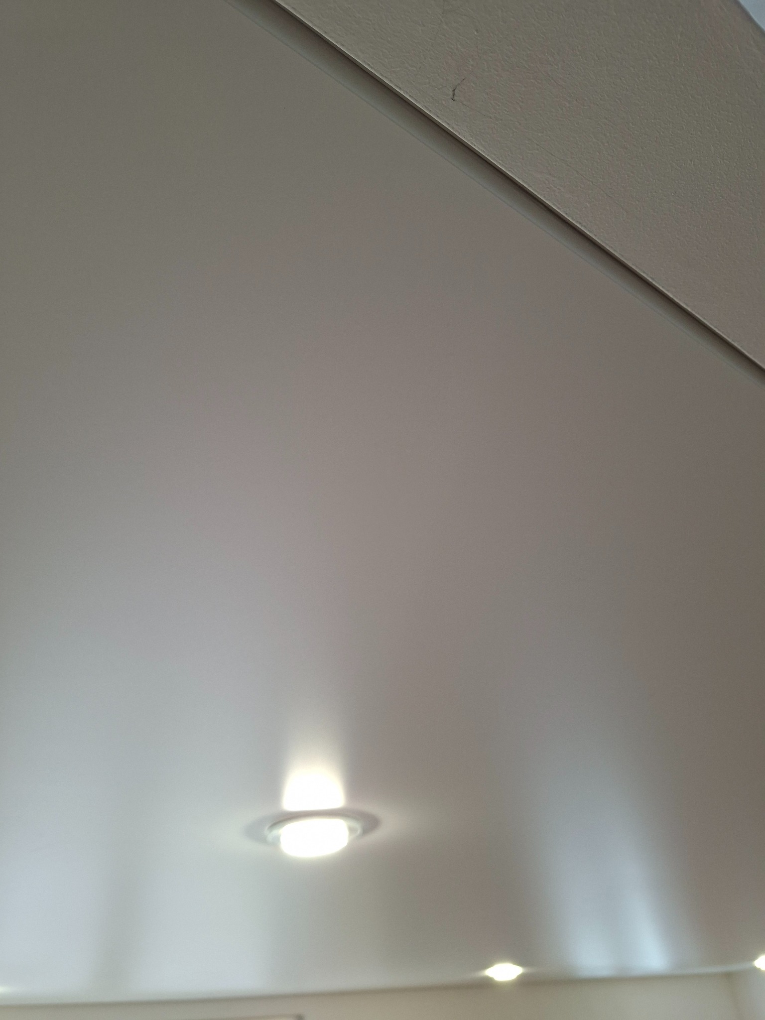 Gładki, kremowy sufit podwieszany z zamontowanymi punktowymi lampami LED, oświetlającymi przestrzeń. Widoczny fragment listwy sufitowej.