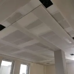 Sufit podwieszany z płyt karton-gips, widoczne łączenia płyt i otwory na oświetlenie, etap szpachlowania przed malowaniem.