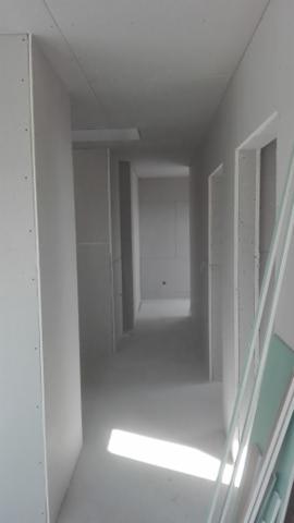 Korytarz w trakcie zabudowy płytami gipsowo-kartonowymi; widoczne profile i płyty opierające się o ścianę, surowe wykończenie, długa perspektywa w głąb.