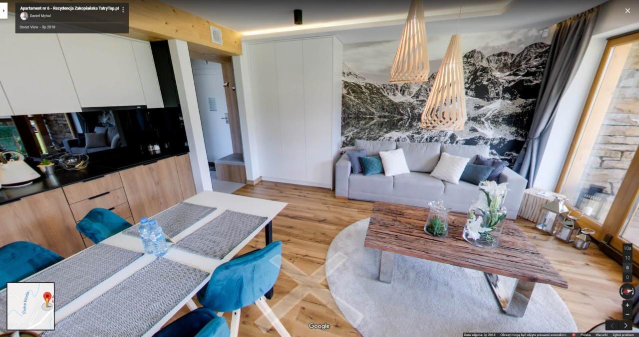 Wnętrze apartamentu w stylu góralskim z drewnianą podłogą, stołem z turkusowymi krzesłami, sofą z poduszkami i fototapetą z motywem górskim.