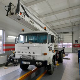 Mila&Trans Sp. z o.o - Biały samochód ciężarowy STAR z podnośnikiem koszowym P183 w warsztacie, widoczny motocykl w tle, tablica rejestracyjna TLW 26GC.