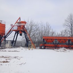 Mila&Trans Sp. z o.o - Pomarańczowa betoniarnia z napisem 'MILA TRANS' na tle zimowego krajobrazu, śnieg na ziemi, widoczne drzewa bez liści.