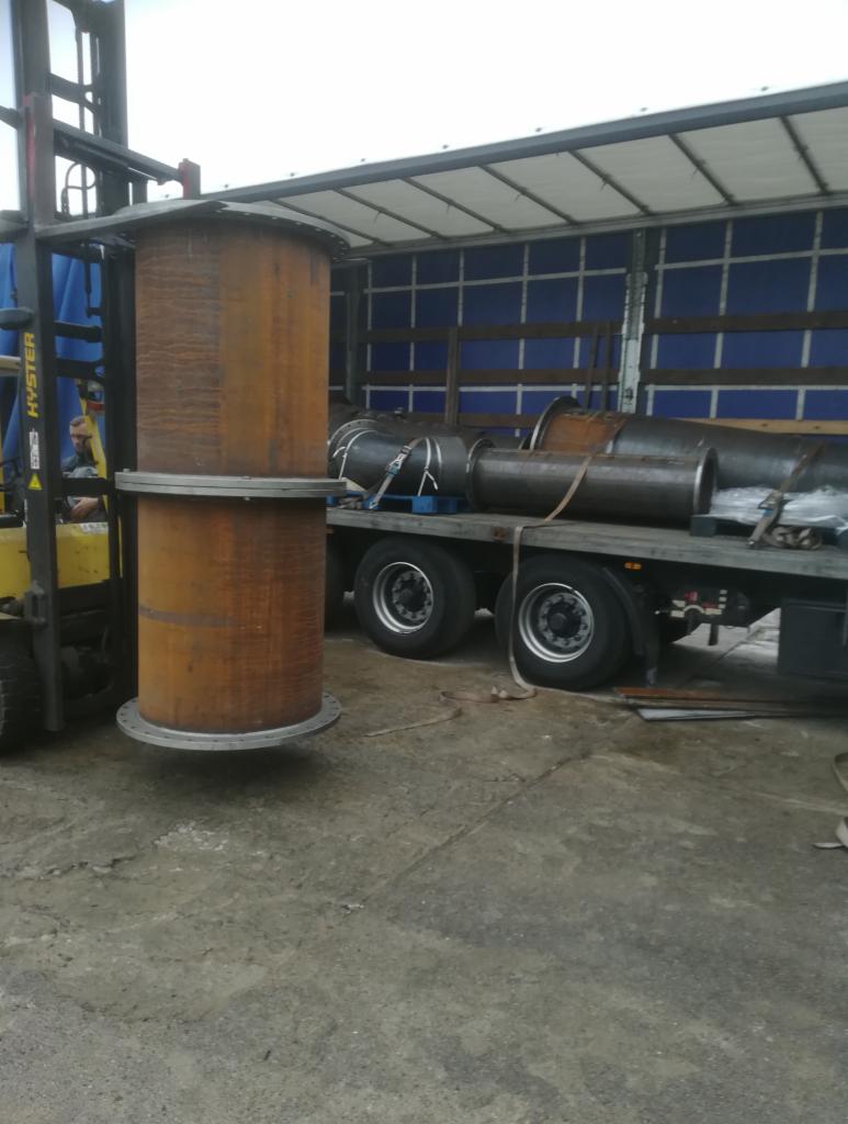 Cylindryczny zbiornik z rdzawej stali podnoszony przez wózek widłowy Hyster na tle ciężarówki z ładunkiem rur