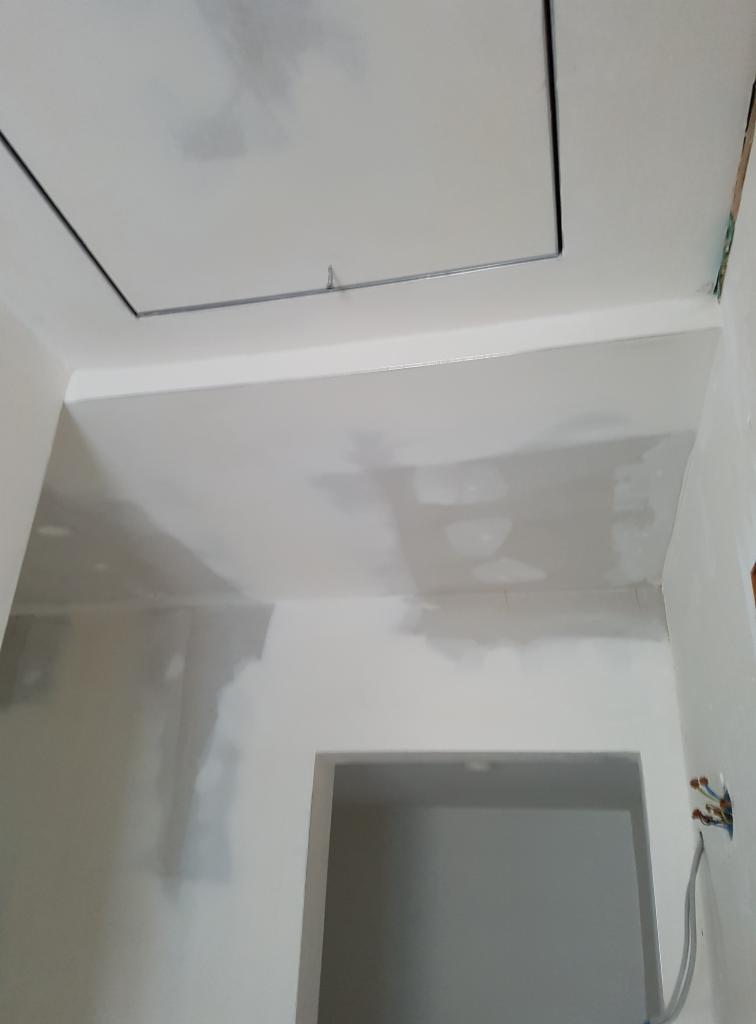 Ściana i sufit w trakcie gładzenia, widoczne ślady szpachli, otwór rewizyjny w suficie, instalacja elektryczna ze zwisającymi przewodami.