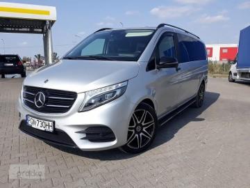 Srebrny Mercedes-Benz V-klasa z czarnymi felgami aluminiowymi, zaparkowany na betonowym placu w słoneczny dzień.