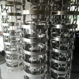 Stosy identycznych, okrągłych, spawanych konstrukcji ze stali nierdzewnej z uchwytami, ustawione na szarym betonowym podłożu w warsztacie.