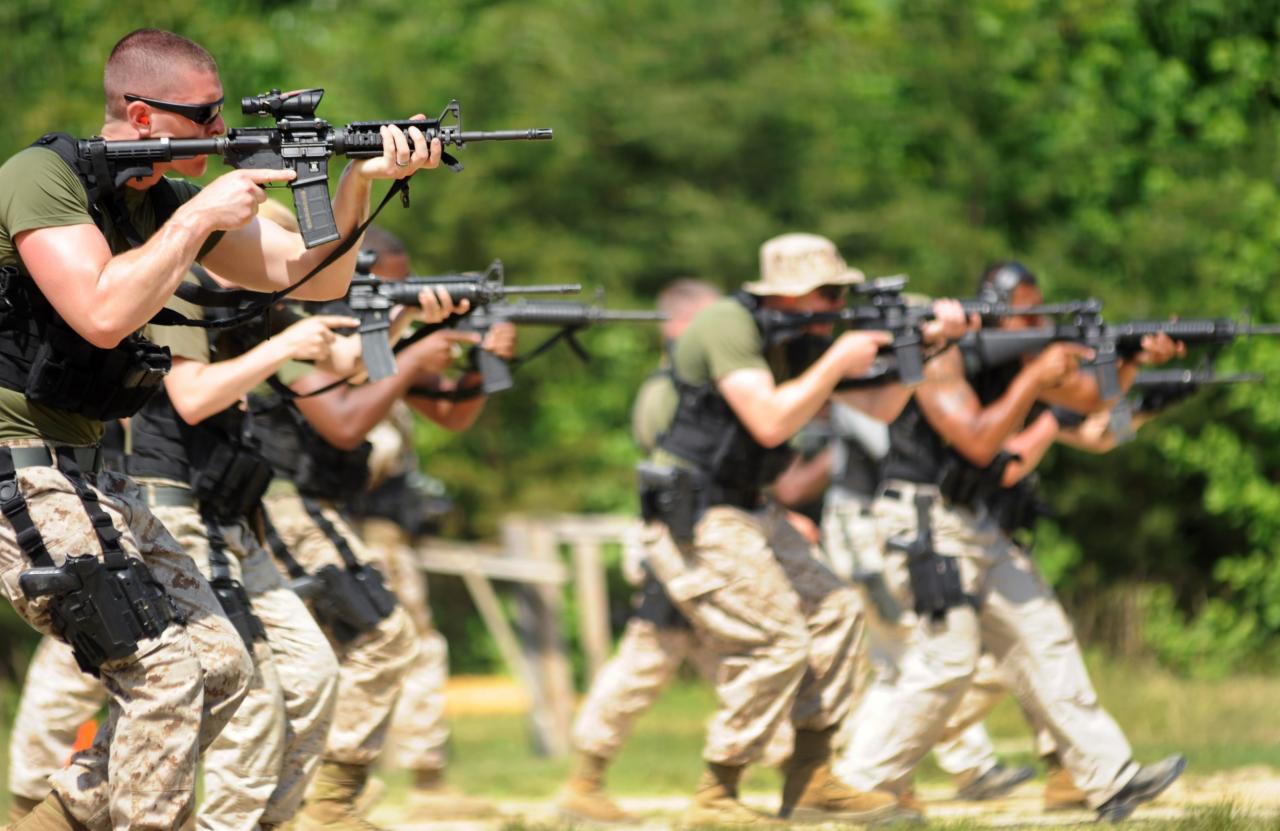 Grupa mężczyzn w kamuflażu, z bronią, podczas ćwiczeń taktycznych na zewnątrz, z zielonym tłem drzew.