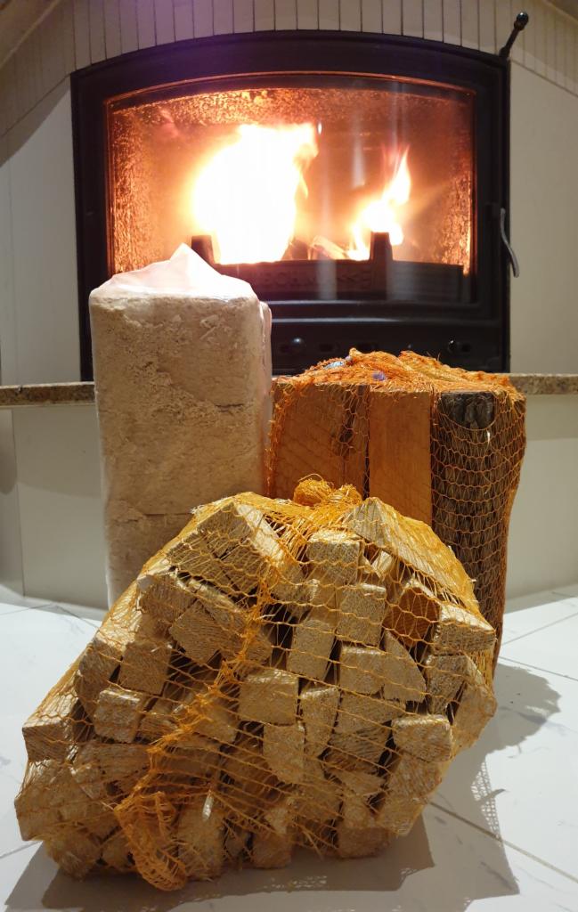 Brykiet drzewny w siatkach i walec z trocin na tle płonącego kominka.