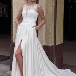 Panna młoda w białej sukni ślubnej z koronkową górą i wysokim rozcięciem na tle kolumny budynku.