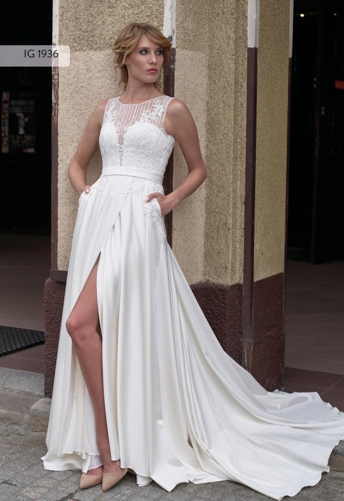 Panna młoda w białej sukni ślubnej z koronkową górą i wysokim rozcięciem na tle kolumny budynku.