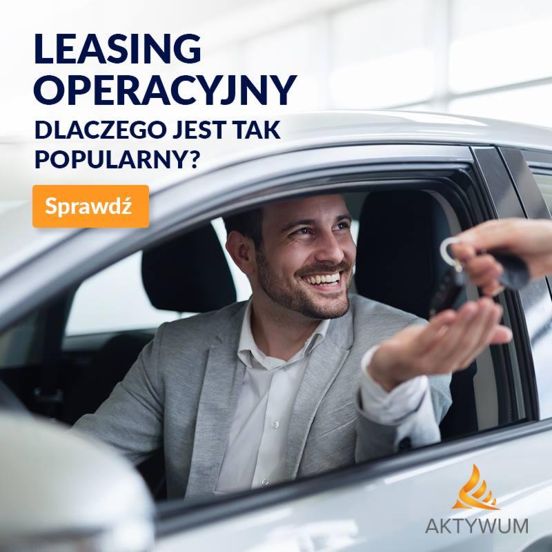 Uśmiechnięty mężczyzna w szarej marynarce siedzi w samochodzie, otrzymując kluczyki od auta.