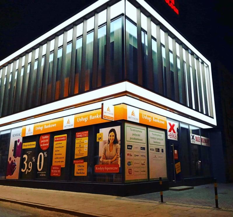 Fasada budynku z reklamami usług bankowych, w tym kredytów hipotecznych i pożyczek pozabankowych, widoczne logo 'AktywuM' i hasła reklamowe.
