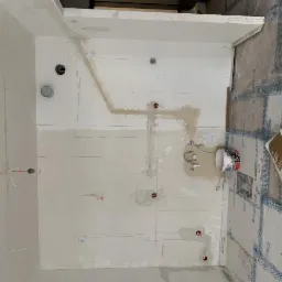 Przygotowanie ścian do wykończenia: widok z góry na wnętrze w trakcie remontu, ściany z widocznymi śladami po instalacjach, częściowo zagruntowane, zarysowane linie pod gniazdka, na podłodze folia...