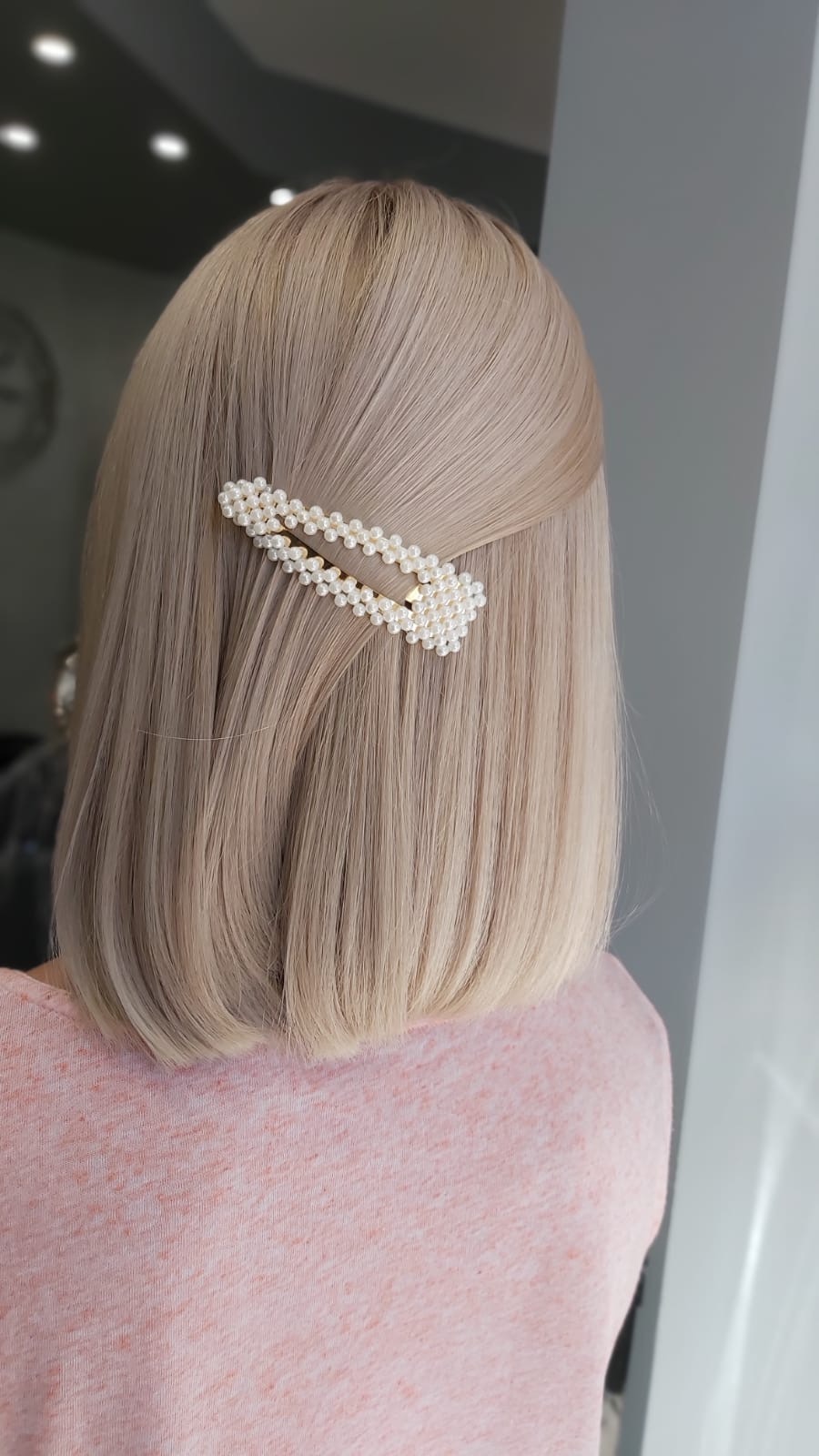 Jasne, proste włosy do ramion z ozdobną spinką w kształcie prostokąta, zdobioną perełkami.