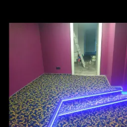 Fioletowe ściany w pokoju z dywanem w złote wzory i podświetlanymi schodami, widoczna drabina w tle.