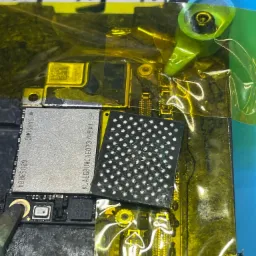 Zbliżenie na płytę główną smartfona z układami scalonymi, w trakcie naprawy, zabezpieczoną żółtą taśmą kaptonową, widoczne oznaczenia układów Samsung i KLAEG8UWCAE0T3746A1 SP.