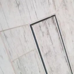 Ułożone jasne panele podłogowe z widocznymi fugami i odpływem liniowym, imitujące strukturę drewna z wyraźnymi słojami.