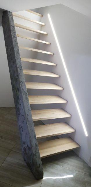 Schody drewniane z betonową belką nośną i oświetleniem LED przy ścianie, widok z dołu.