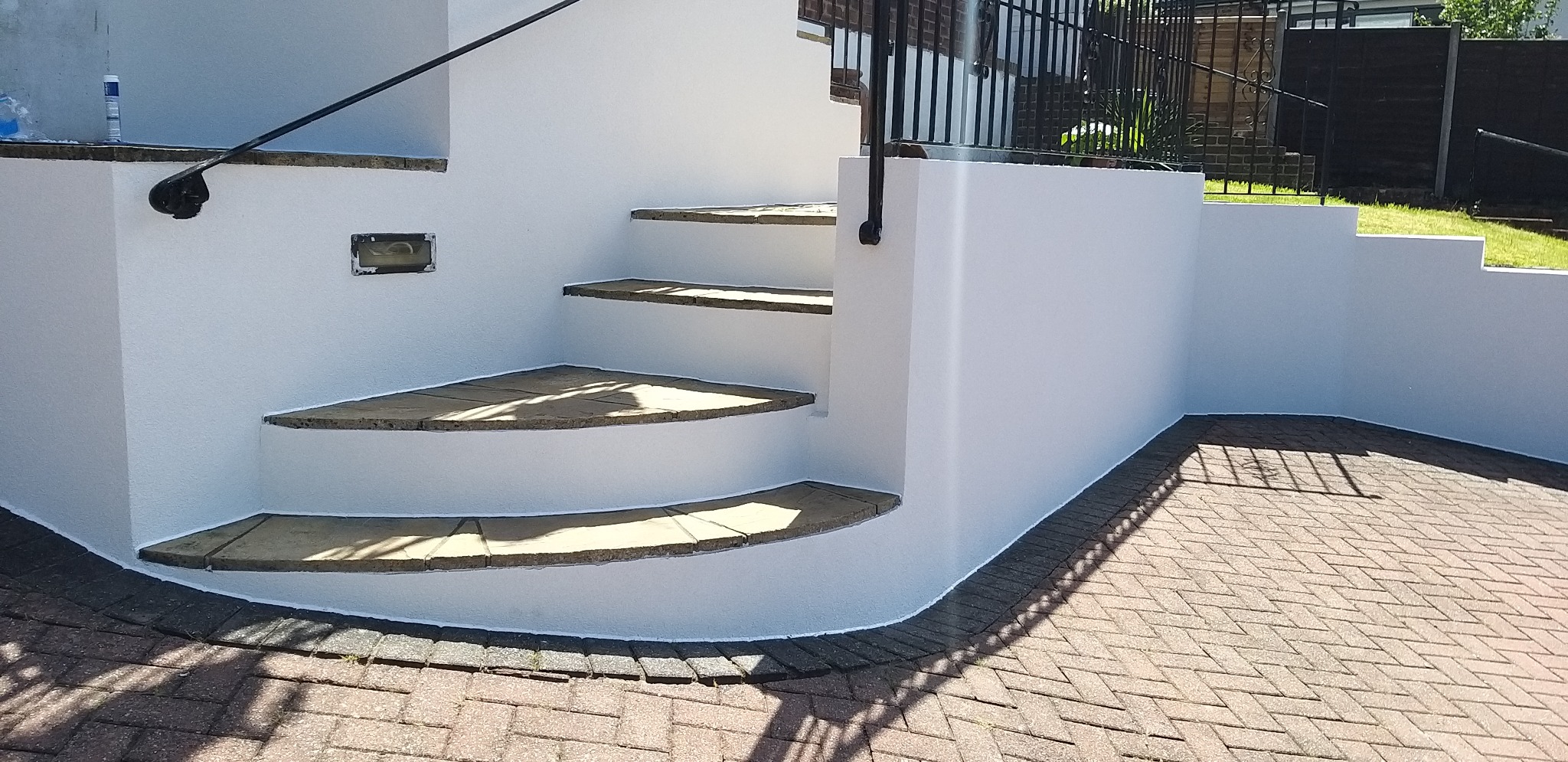 Białe, odnowione schody zewnętrzne z kamiennymi stopniami i czarną balustradą, otoczone brukowaną nawierzchnią. Świeżo pomalowane ściany i precyzyjne wykończenia.