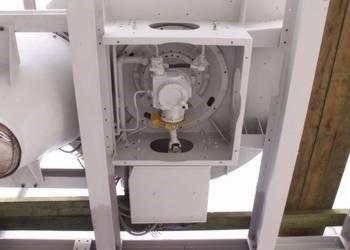 Wnętrze białej, metalowej obudowy maszyny z widocznymi elementami hydraulicznymi i przewodami, ujęcie z dołu.