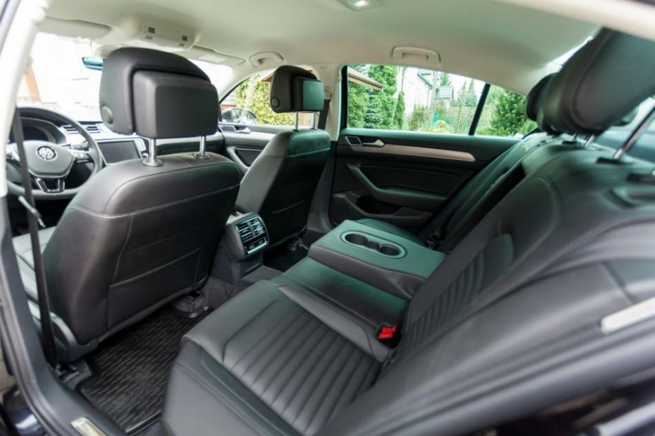 Wnętrze samochodu osobowego z czarną skórzaną tapicerką, widok na tylną kanapę z podłokietnikiem i uchwytami na napoje oraz regulowane zagłówki