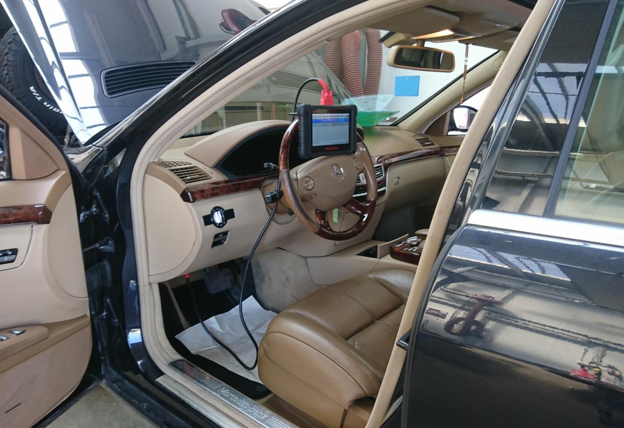Wnętrze luksusowego samochodu Mercedes-Benz podczas diagnostyki komputerowej, z podłączonym urządzeniem diagnostycznym do kierownicy.