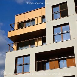 INWERSA Edyta Werkowska - Nowoczesny budynek mieszkalny z balkonami i dużymi oknami, odbijającymi błękitne niebo. Ujęcie z dołu podkreśla geometrię fasady i detale architektoniczne.