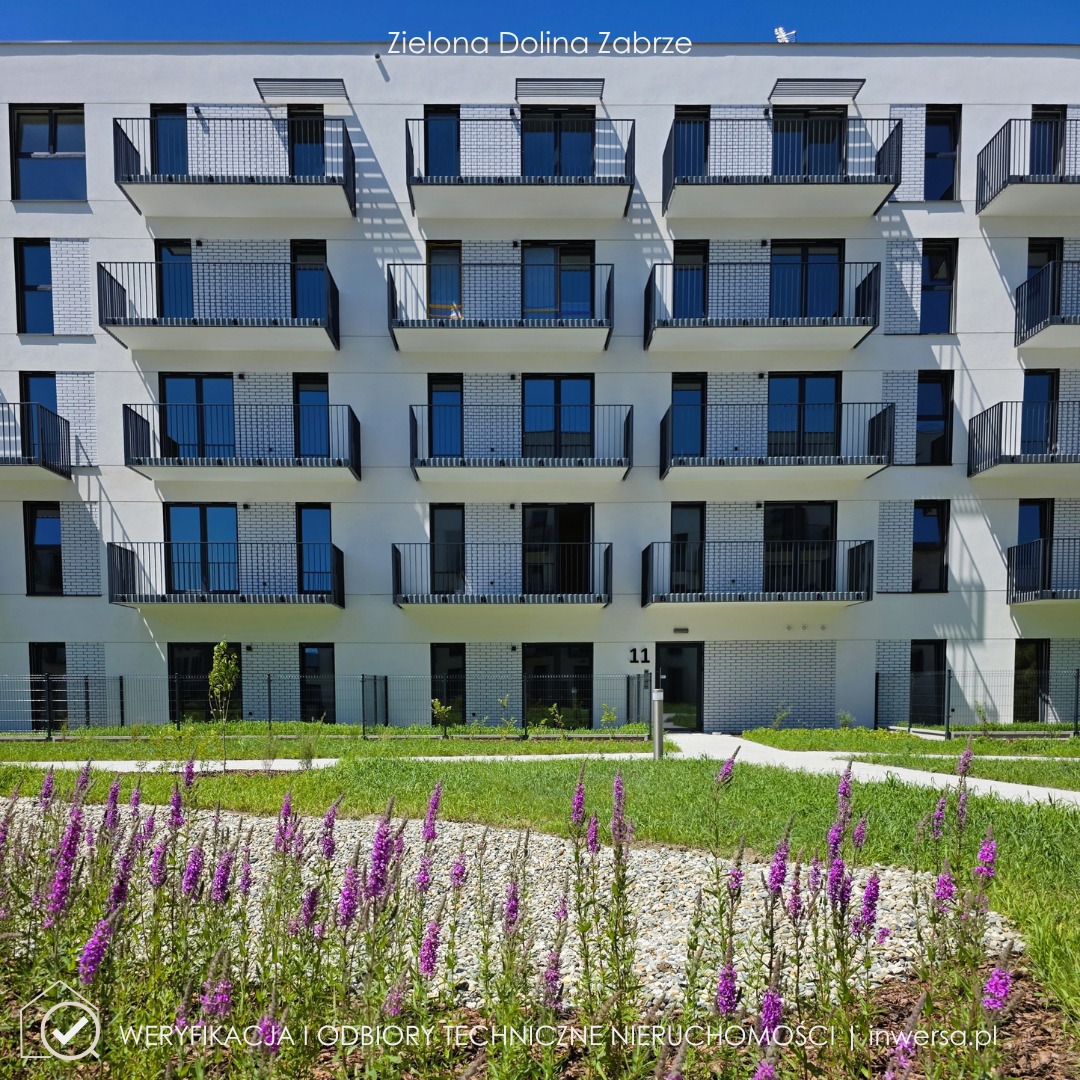 Nowoczesny budynek apartamentowy z balkonami i zielonym otoczeniem. Widoczne fioletowe kwiaty na pierwszym planie i numer 11 nad wejściem. Fasada w jasnej kolorystyce.