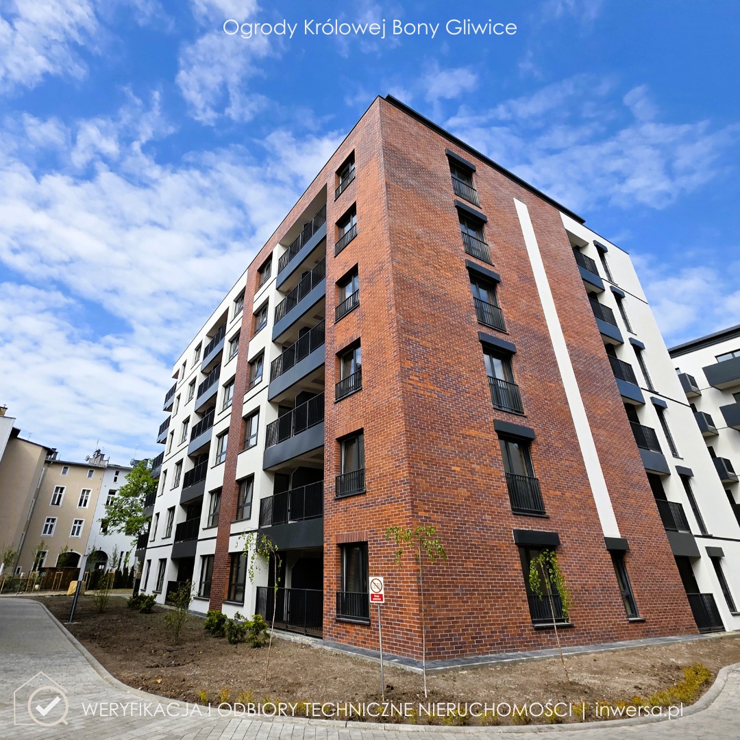 Nowoczesny budynek mieszkalny z ceglaną elewacją i balkonami, widoczny z dołu pod błękitnym niebem. Na pierwszym planie trawnik i chodnik z kostki brukowej.