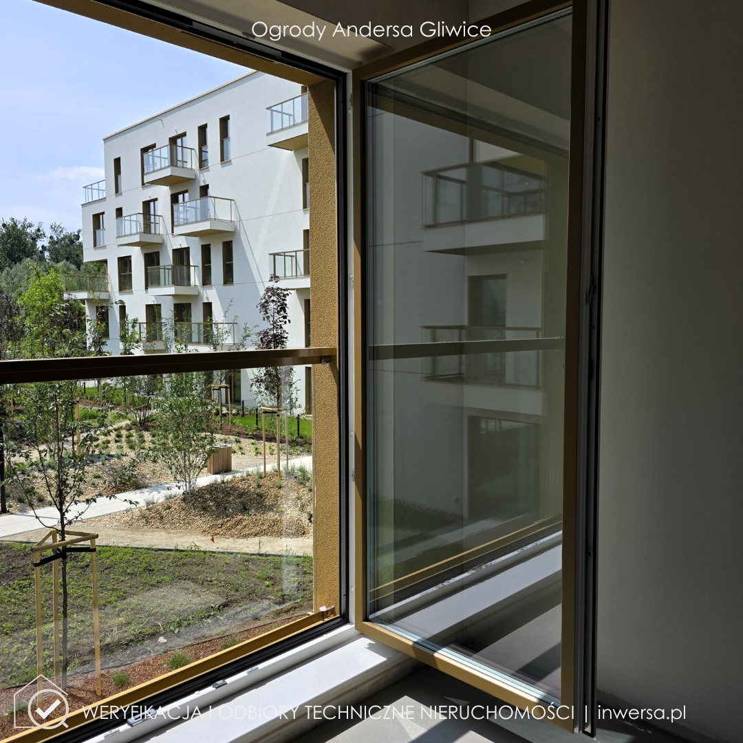 Widok z okna na nowoczesny apartamentowiec 'Ogrody Andersa' w Gliwicach, z uwzględnieniem detali stolarki okiennej i zagospodarowania terenu zielonego.