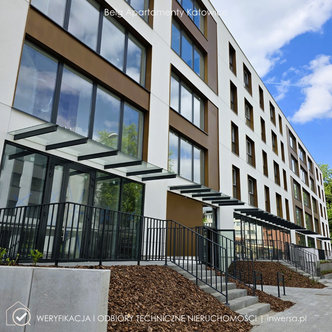 Nowoczesny budynek apartamentowy z brązowo-białą elewacją, szklanymi zadaszeniami nad wejściami i schodami z czarnymi barierkami. Błękitne niebo w tle.