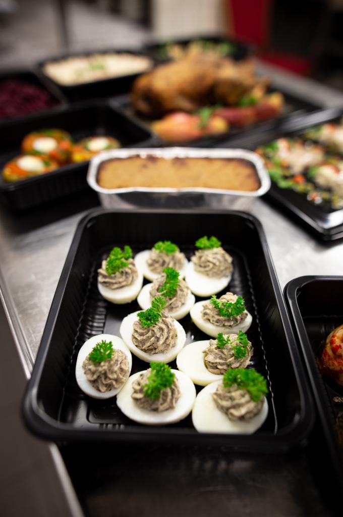 Jajka faszerowane w czarnym pojemniku z dekoracją z zielonej pietruszki, w tle inne dania gotowe do serwowania.