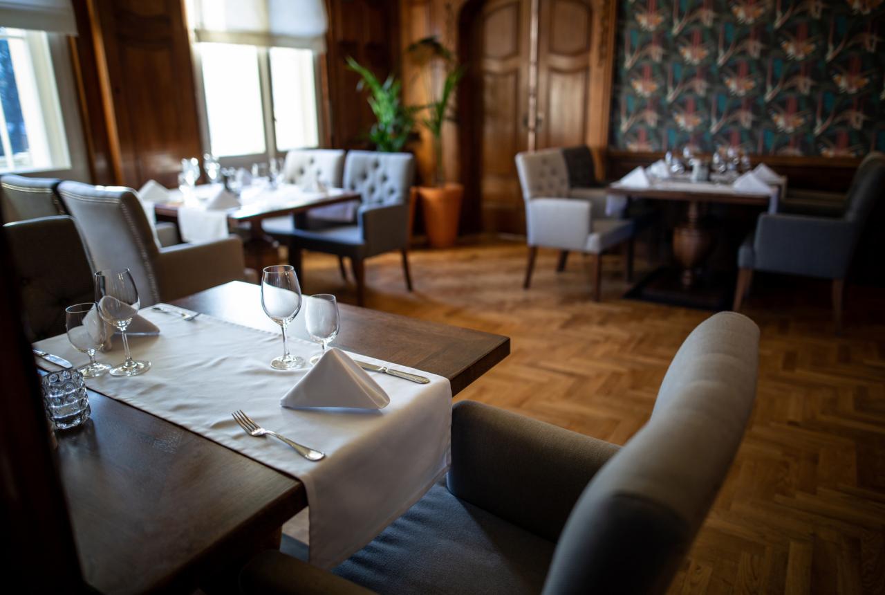 Elegancko nakryty stół z białym bieżnikiem, kieliszkami i sztućcami w stylowym wnętrzu restauracji z parkietem w jodełkę i tapetą w geometryczne wzory.