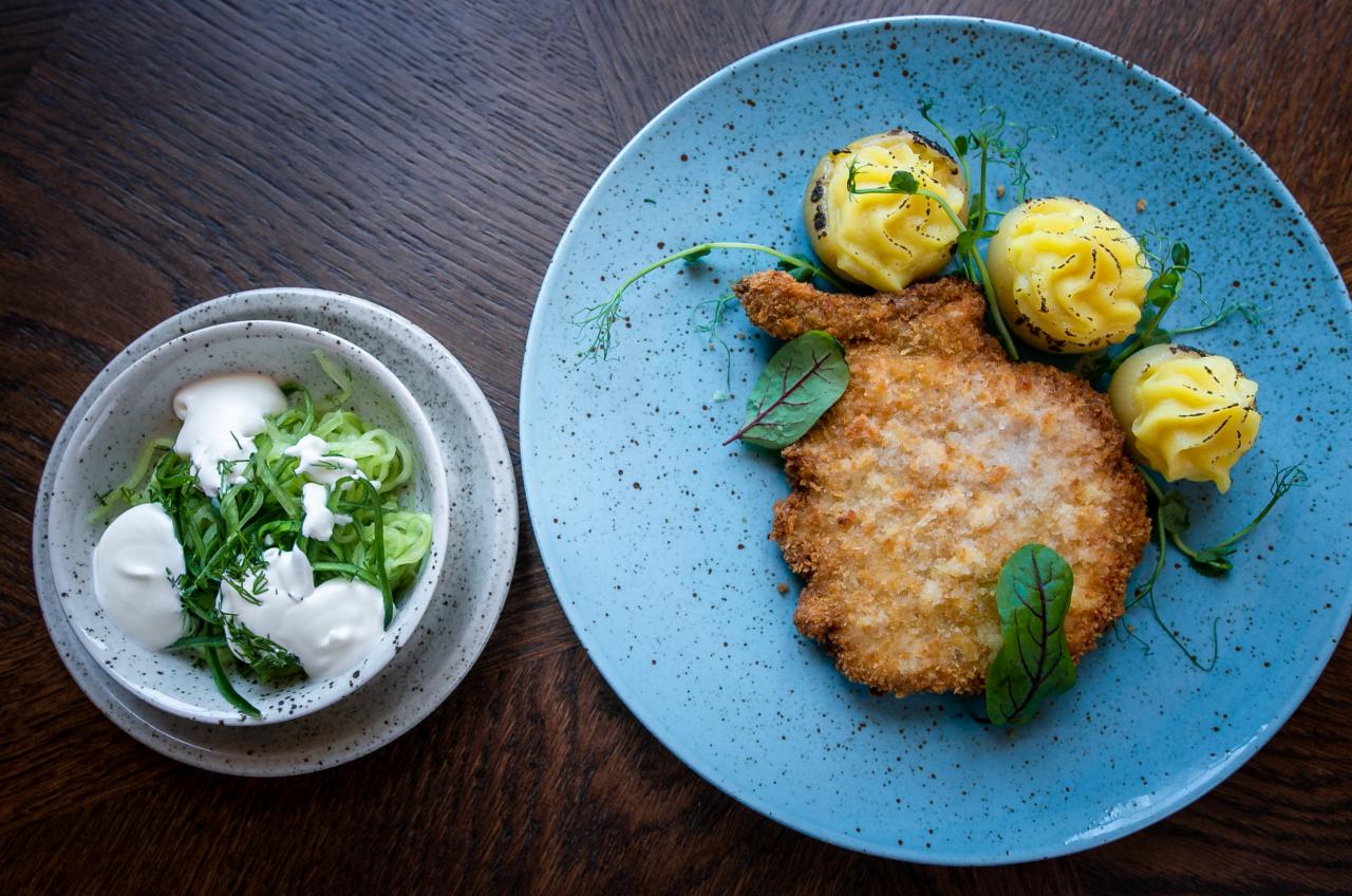 Kotlet schabowy z ziemniakami puree i mizerią podany na niebieskim talerzu.