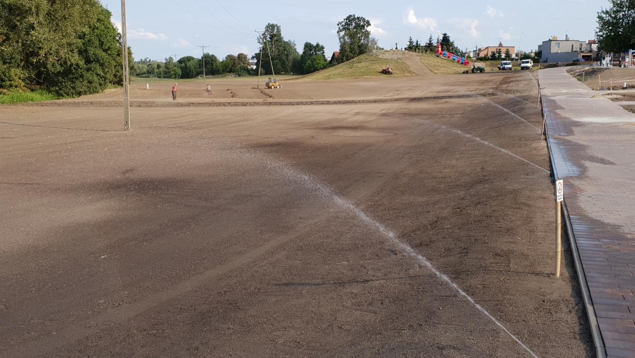 Automatyczne nawadnianie nowo założonego trawnika z widocznymi zraszaczami, w tle prace ziemne i przygotowanie terenu pod zieleń.