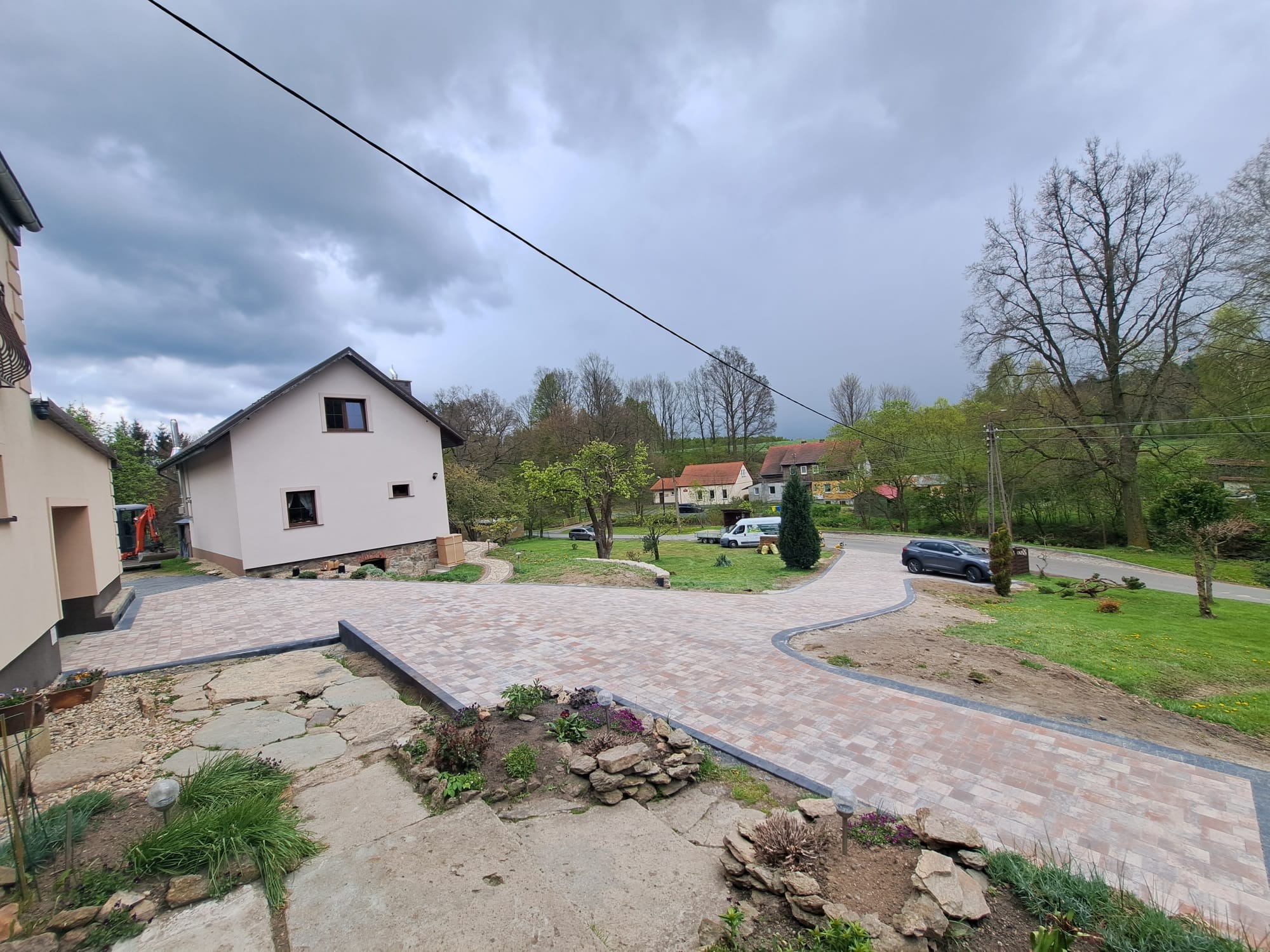 Nowa, kręta ścieżka z kostki brukowej prowadząca do domu z ogrodem, widok z góry, pochmurne niebo w tle.
