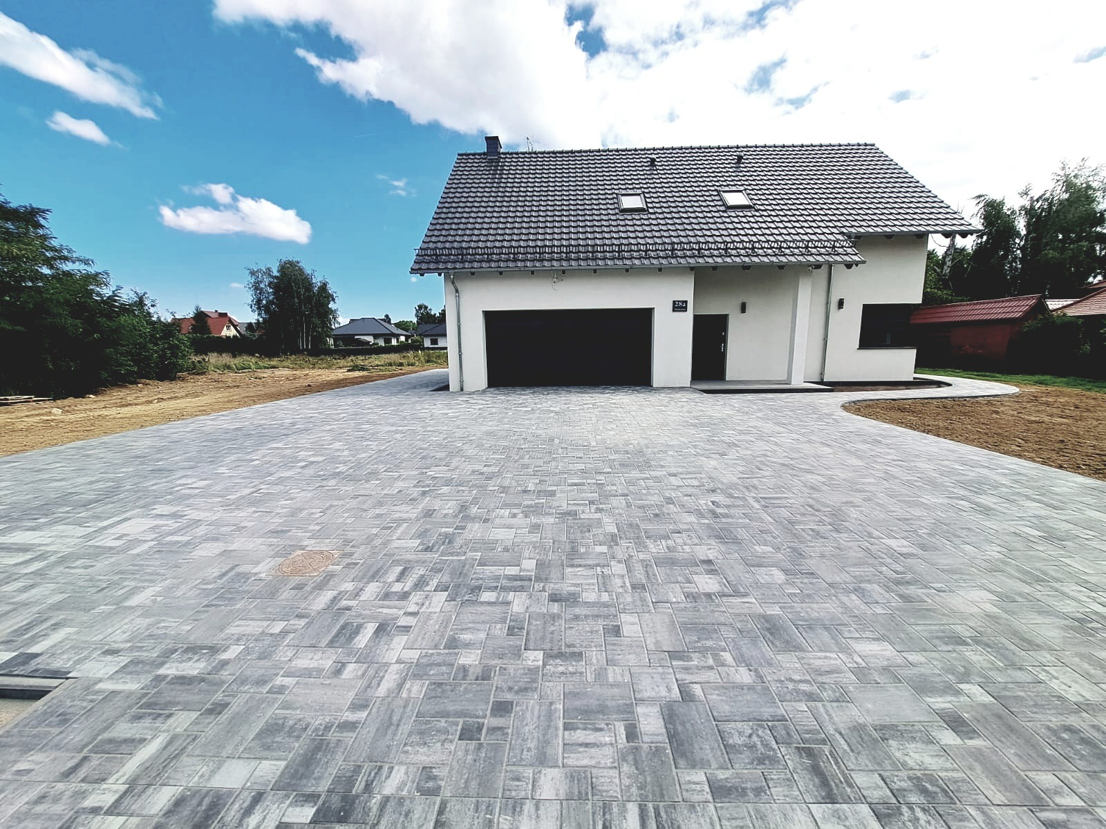 Nowoczesny podjazd z szarej kostki brukowej ułożonej we wzór patchworkowy przed domem w Gryfowie Śląskim, widok z poziomu gruntu.